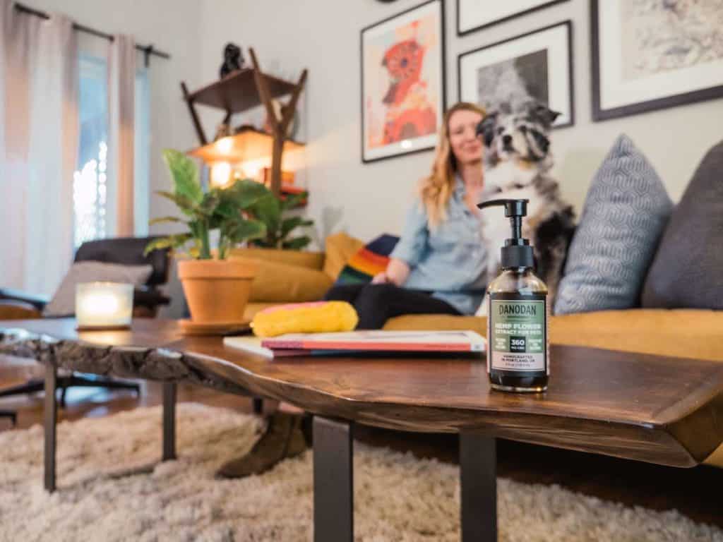Dog and woman sit on couch with bottle of Danodan Hemp Extract for Pets on the coffee table