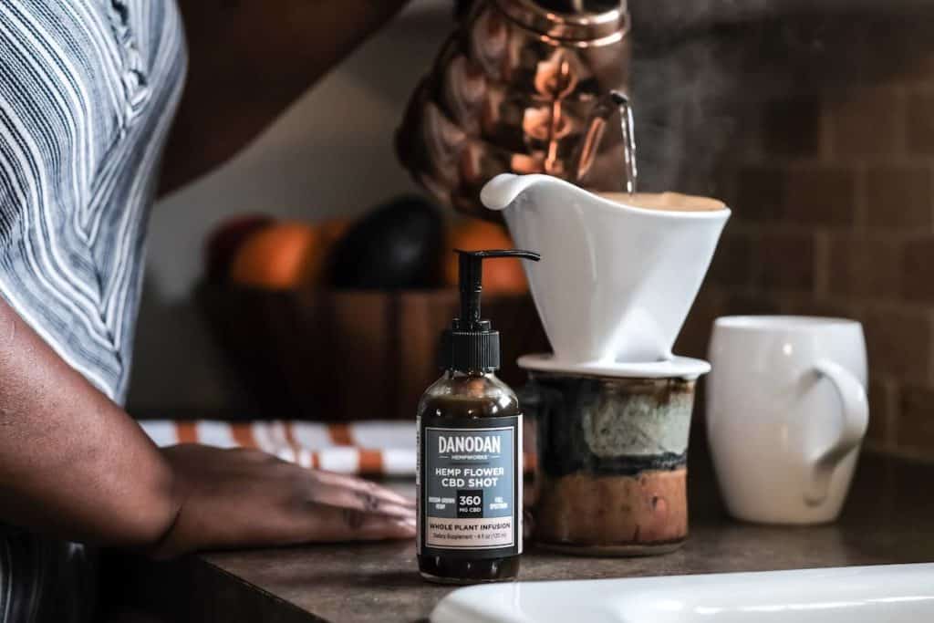 A woman makes a cup of pour-over coffee with a bottle of Danodan CBD.