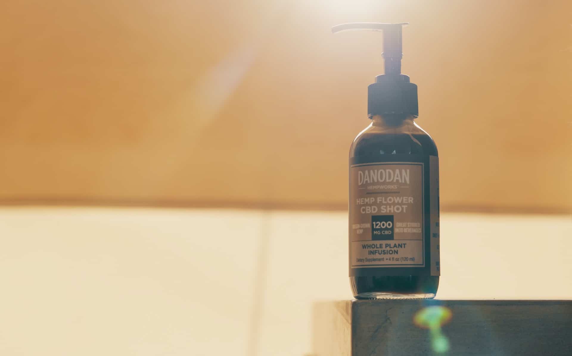 A closeup of a 4oz bottle of Danodan 1200mg CBD with a sunburst behind it.